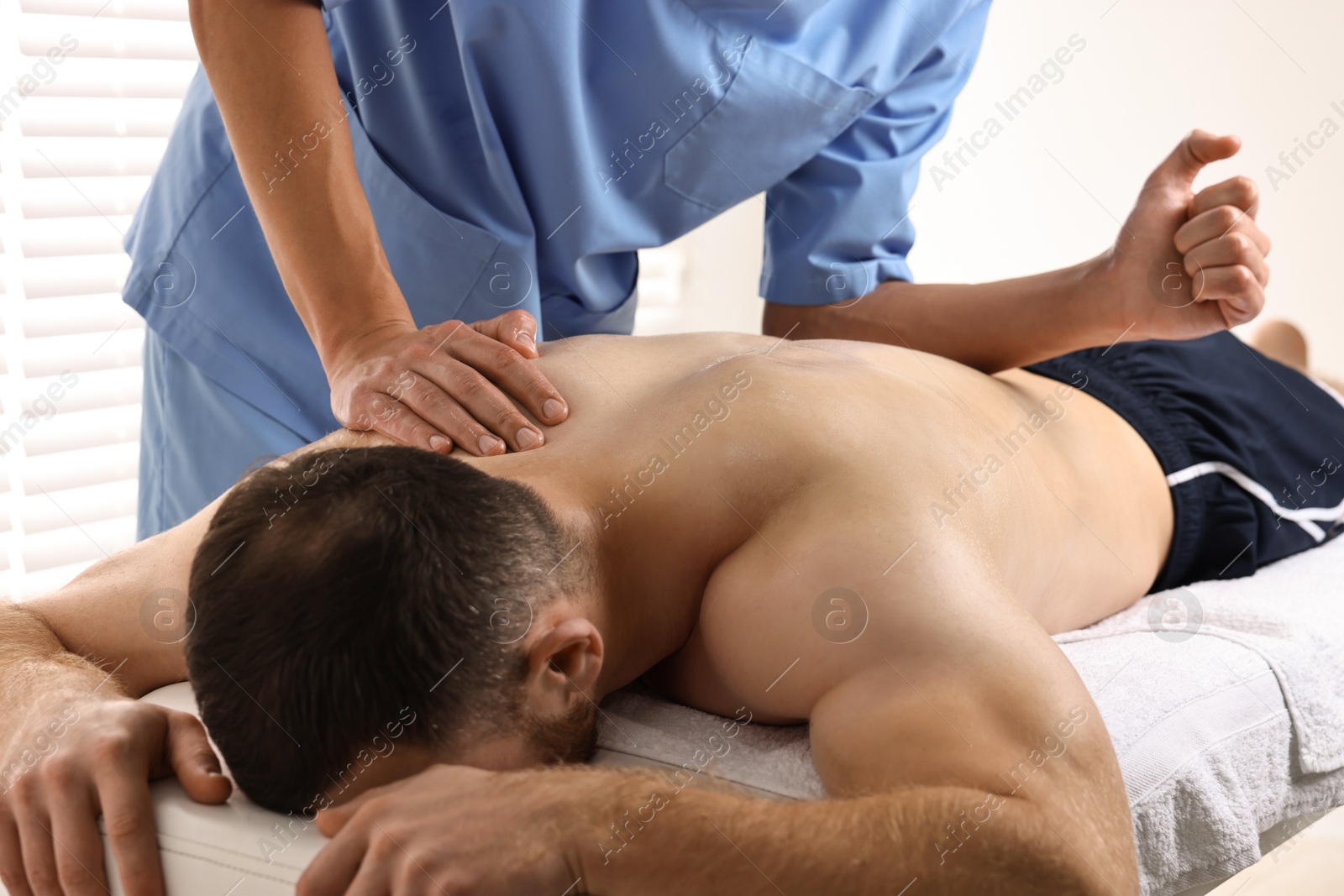 Photo of Professional physiotherapist doing back massage for his client indoors, closeup