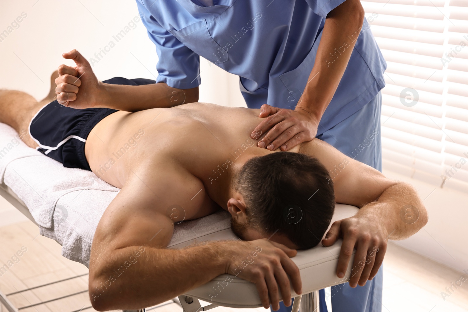 Photo of Professional physiotherapist doing back massage for his client indoors, closeup