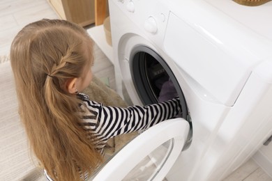 Photo of Little helper. Cute girl doing laundry at home, above view