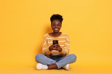 Photo of Happy woman with smartphone on yellow background