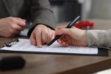 Photo of Manager and client signing car purchase agreement at wooden table, selective focus. Buying auto