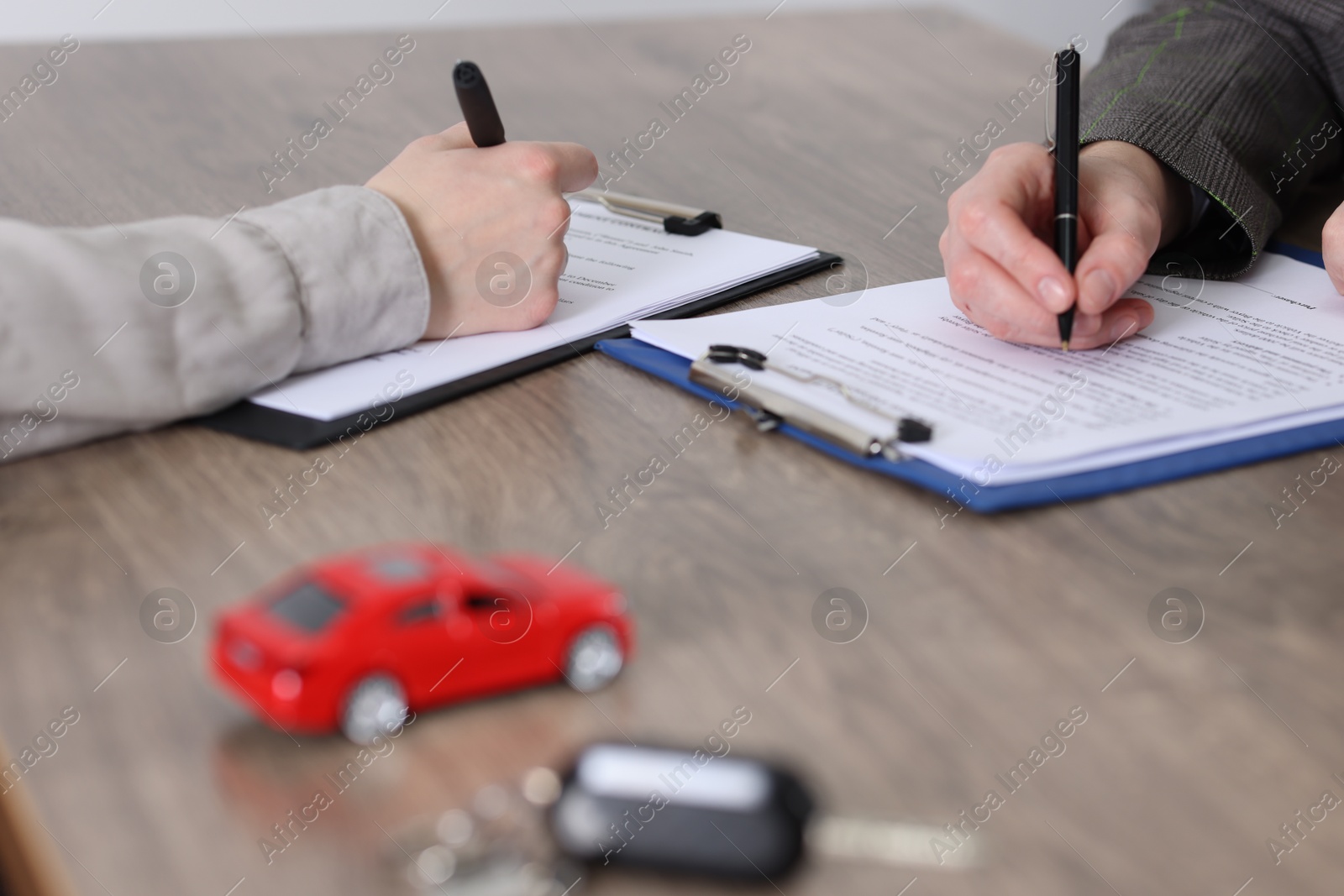 Photo of Manager and client signing car purchase agreement at wooden table, selective focus. Buying auto