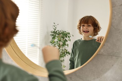 Cute boy brushing his teeth near mirror at home