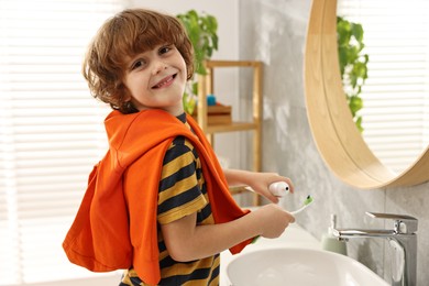 Photo of Cute boy applying paste on toothbrush in bathroom