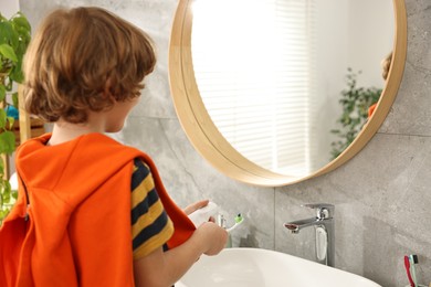 Photo of Cute boy applying paste on toothbrush in bathroom