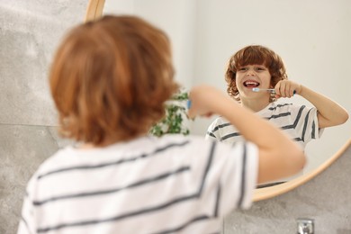 Cute boy brushing his teeth near mirror in bathroom, selective focus