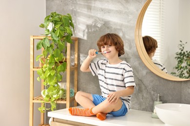 Photo of Cute boy brushing his teeth on countertop in bathroom