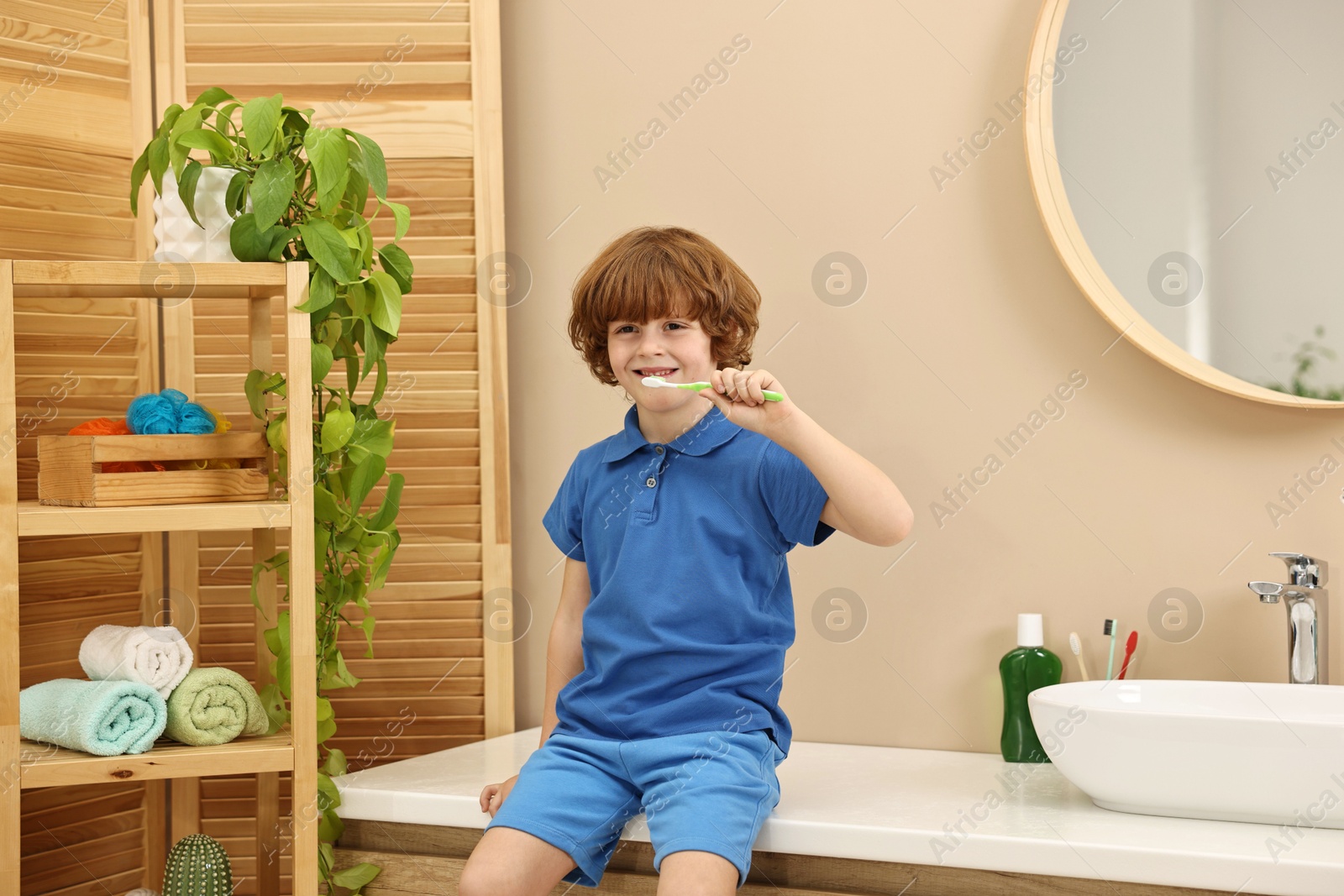 Photo of Cute boy brushing his teeth on countertop in bathroom