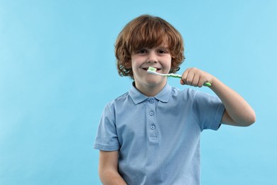 Photo of Cute boy brushing his teeth on light blue background