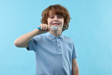 Cute boy brushing his teeth on light blue background