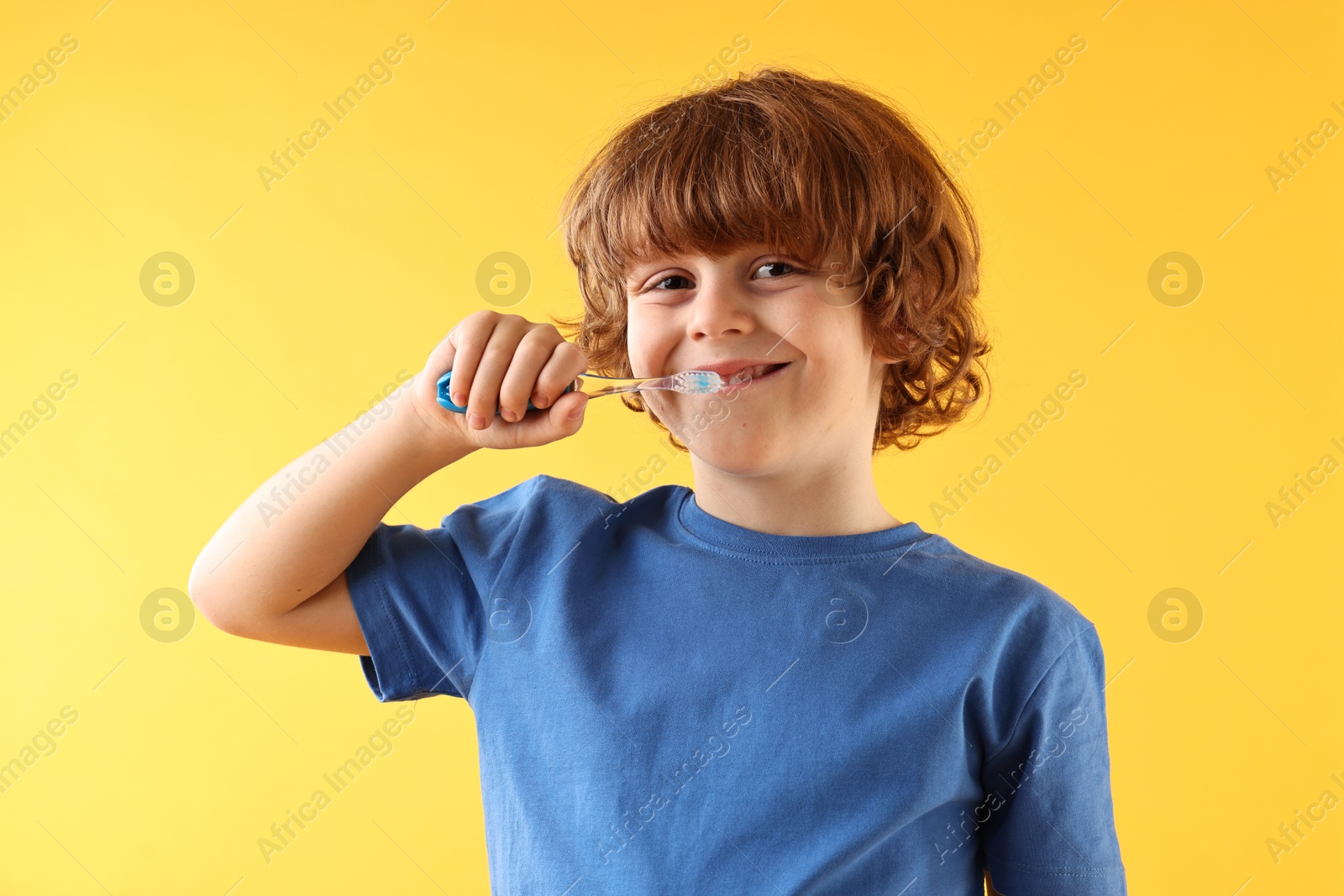 Photo of Cute boy brushing his teeth on yellow background