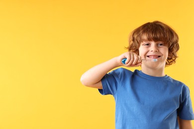 Cute boy brushing his teeth on yellow background, space for text