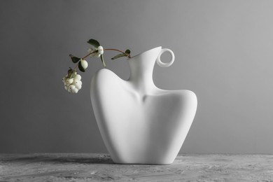 Stylish vase with snowberry branch on grey table