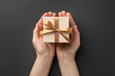 Woman holding gift box with golden bow on black background, top view