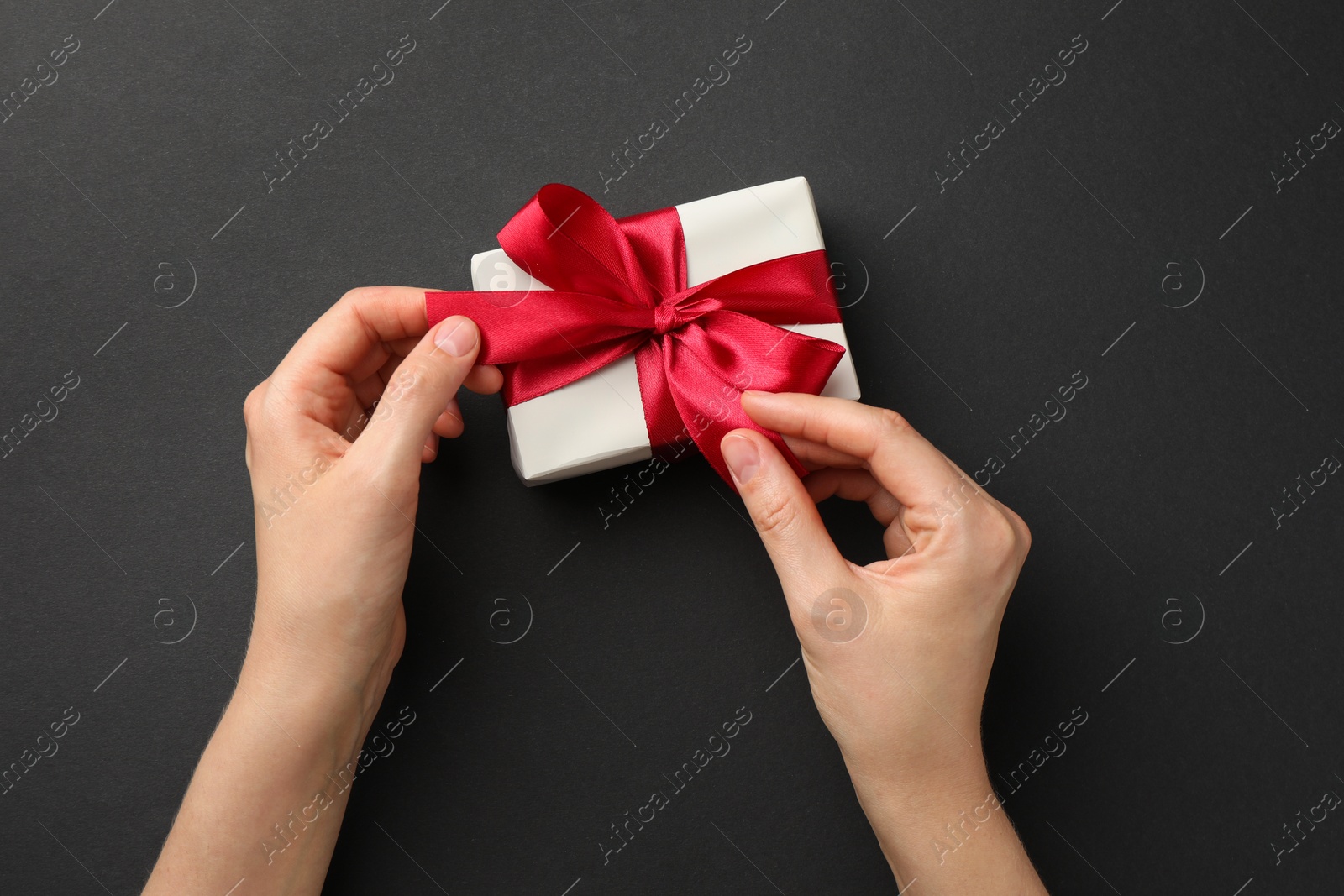 Photo of Woman opening gift box on black background, top view