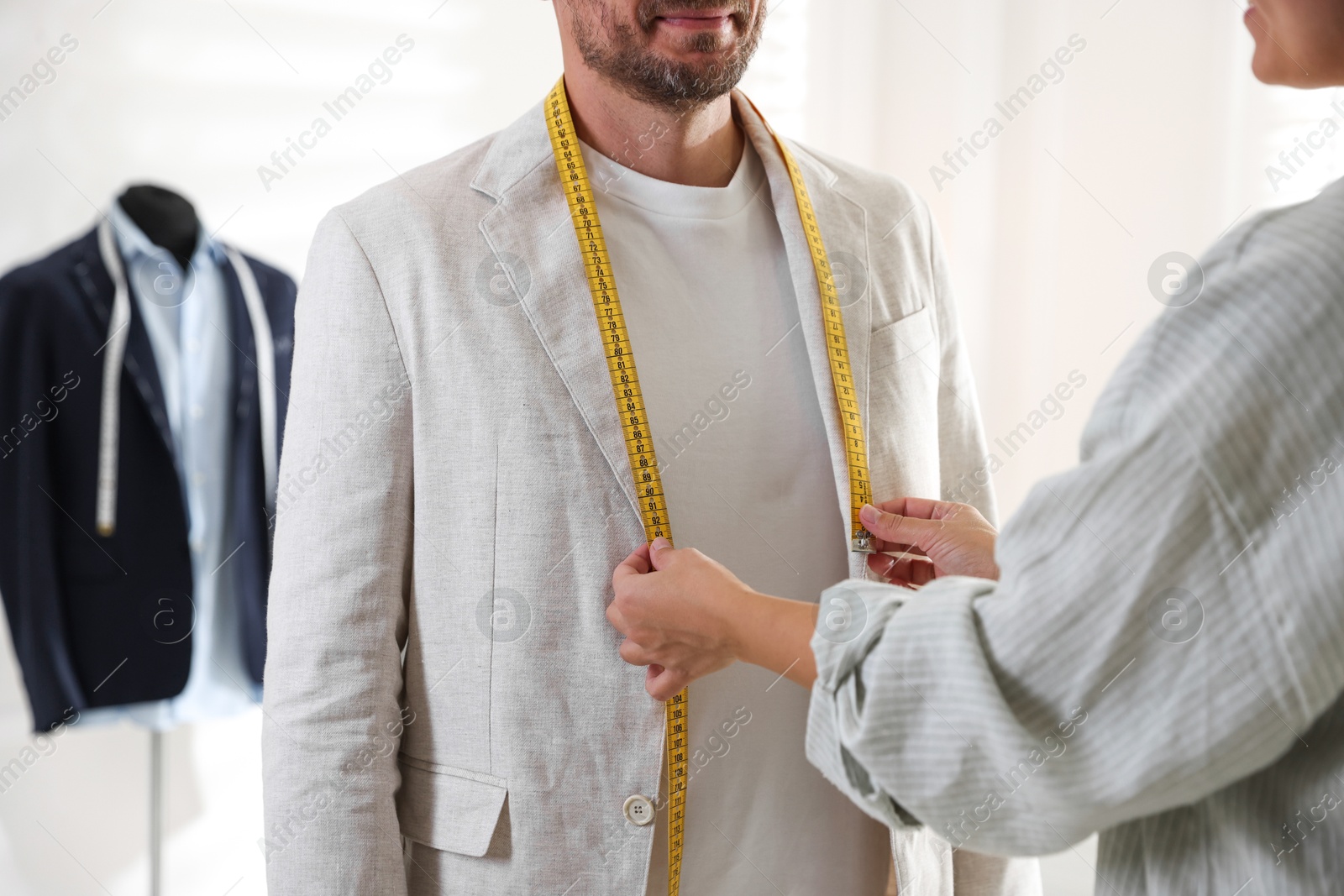 Photo of Woman measuring jacket lapel on man in atelier, closeup