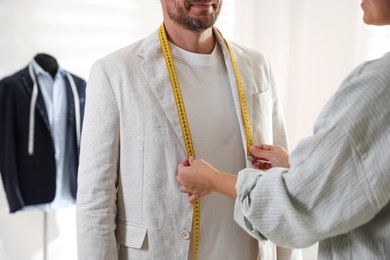 Photo of Woman measuring jacket lapel on man in atelier, closeup