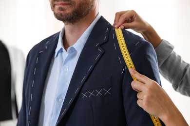 Photo of Tailor measuring jacket on man during fitting in atelier, closeup