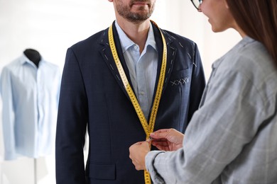 Tailor measuring jacket on man during fitting in atelier, closeup