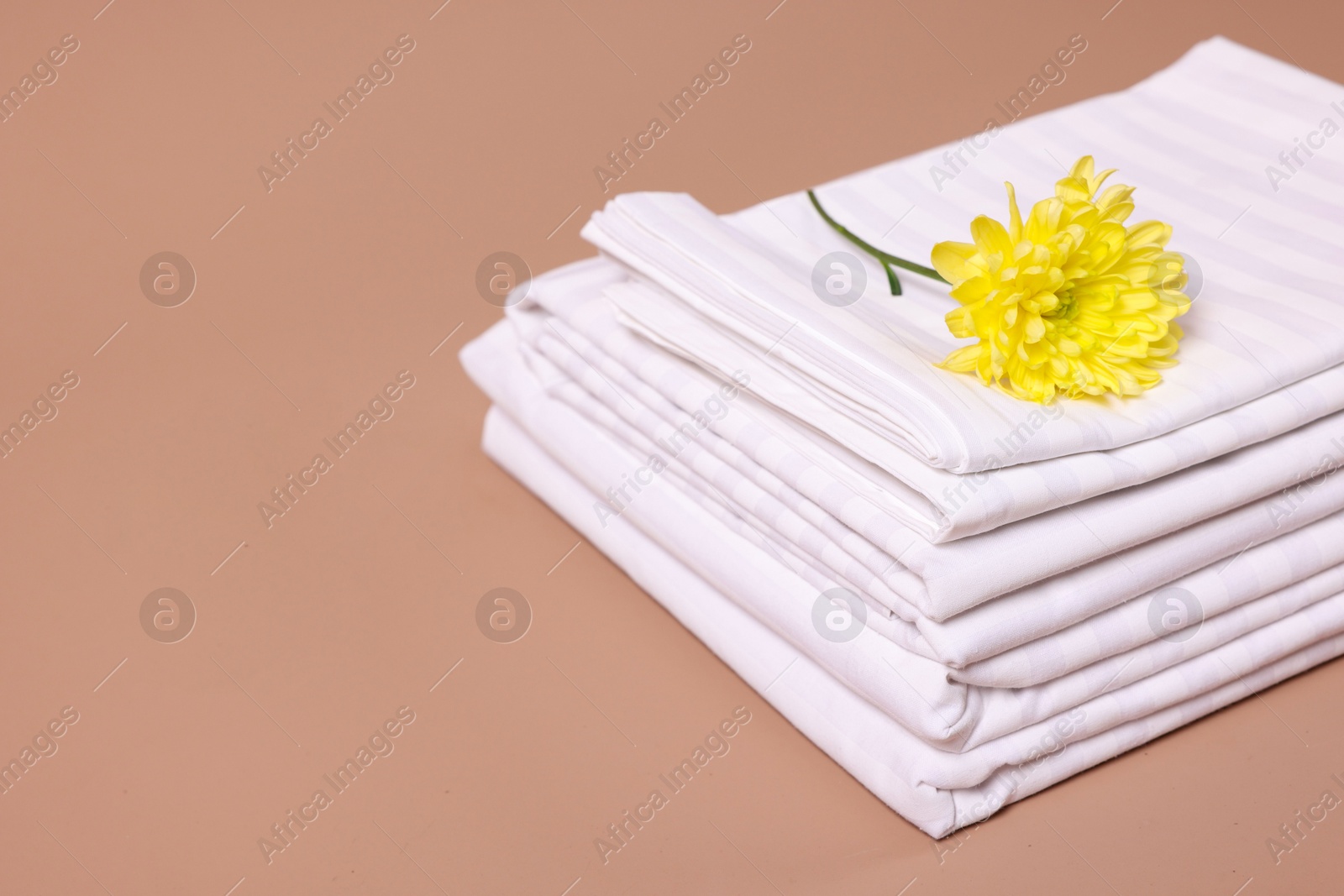 Photo of Stack of clean bed linens and beautiful flower on beige background, closeup. Space for text