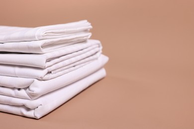 Photo of Stack of clean bed linens on beige background, closeup. Space for text