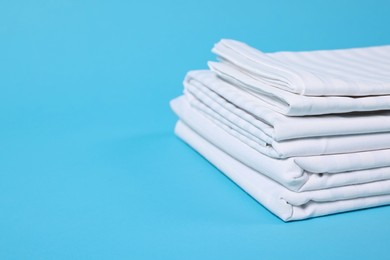 Photo of Stack of clean bed linens on light blue background, closeup. Space for text