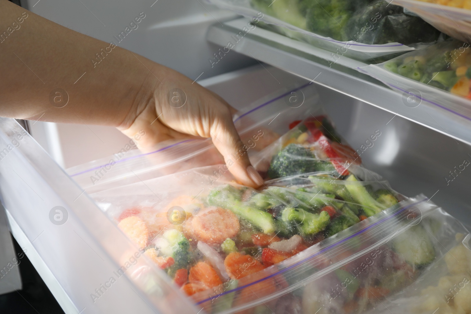 Photo of Woman taking plastic bag with mix of frozen vegetables from refrigerator, closeup