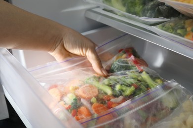 Photo of Woman taking plastic bag with mix of frozen vegetables from refrigerator, closeup