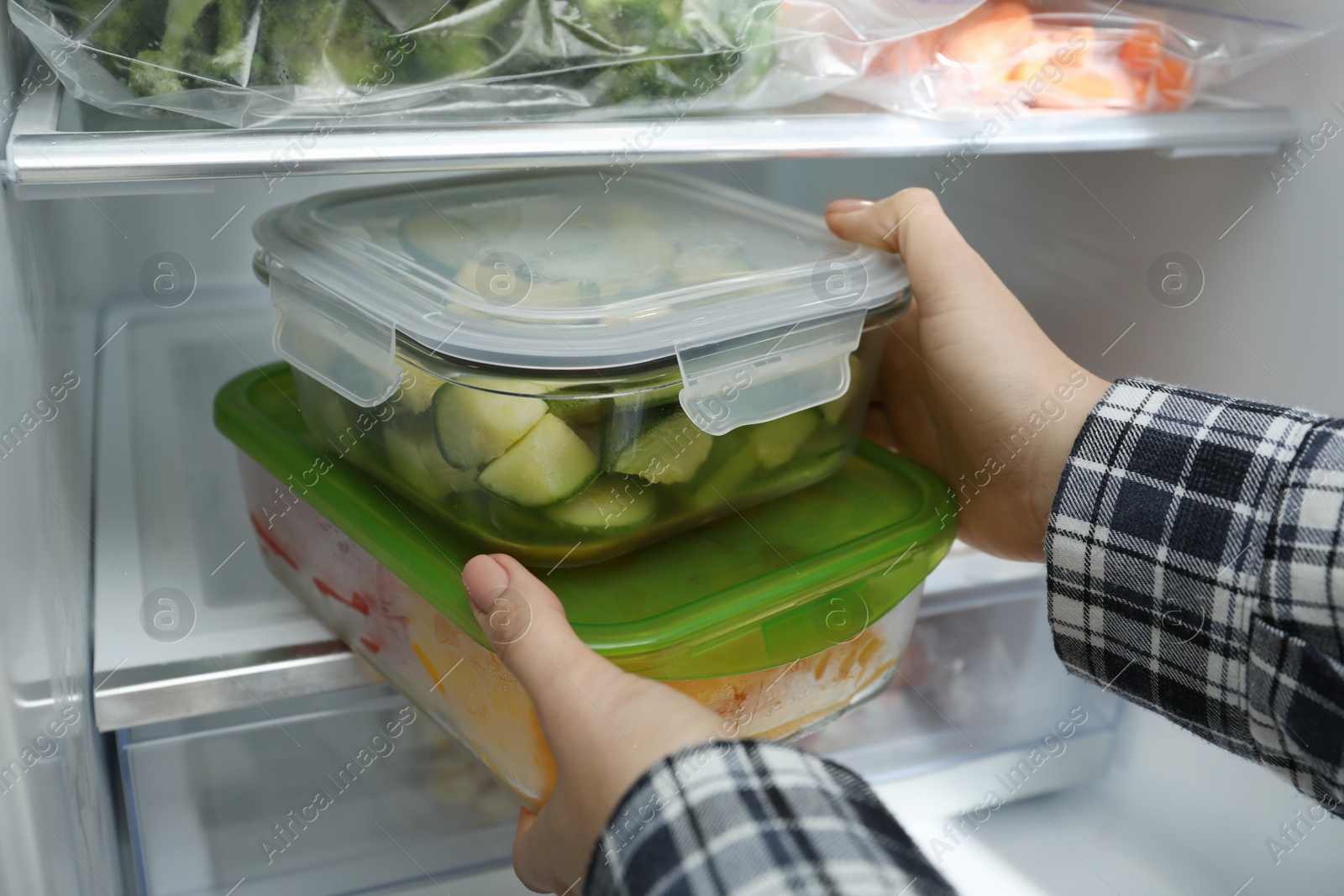 Photo of Woman taking glass containers with frozen vegetables from refrigerator, closeup