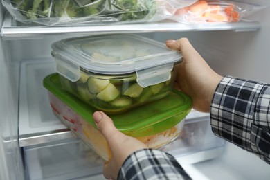 Photo of Woman taking glass containers with frozen vegetables from refrigerator, closeup