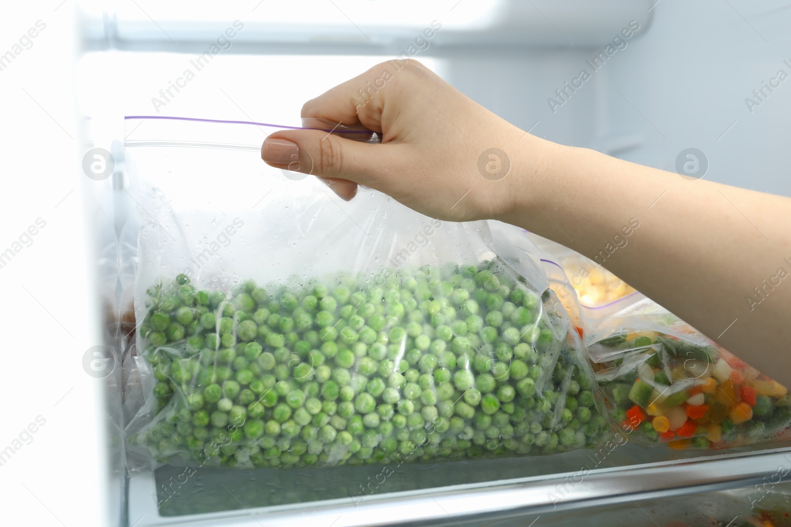 Photo of Woman taking plastic bag with frozen green peas from refrigerator, closeup