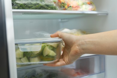 Photo of Woman taking glass container with frozen chopped zucchini from refrigerator, closeup