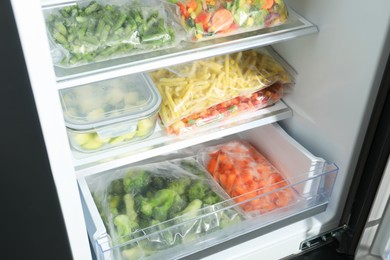 Photo of Plastic bags and glass container with different frozen vegetables in refrigerator