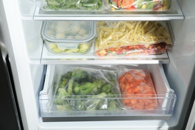 Photo of Plastic bags and glass container with different frozen vegetables in refrigerator