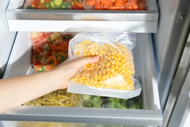 Photo of Woman taking plastic bag with frozen corn kernels from refrigerator, closeup