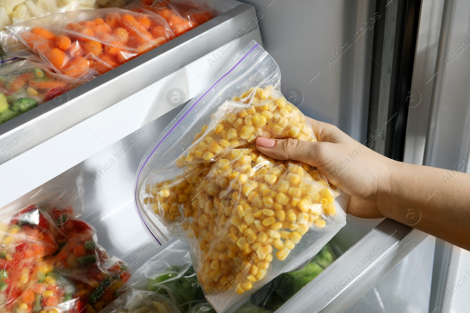 Photo of Woman taking plastic bag with frozen corn kernels from refrigerator, closeup