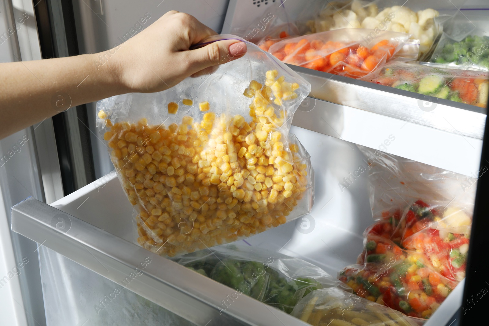 Photo of Woman taking plastic bag with frozen corn kernels from refrigerator, closeup