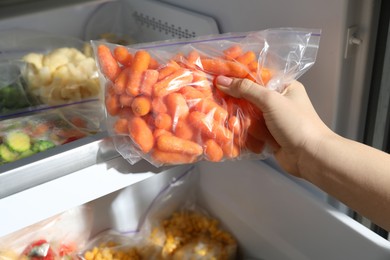 Photo of Woman taking plastic bag with frozen carrots from refrigerator, closeup