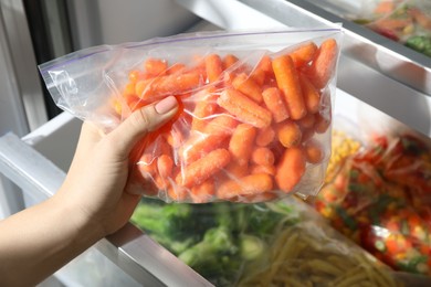 Photo of Woman taking plastic bag with frozen carrots from refrigerator, closeup