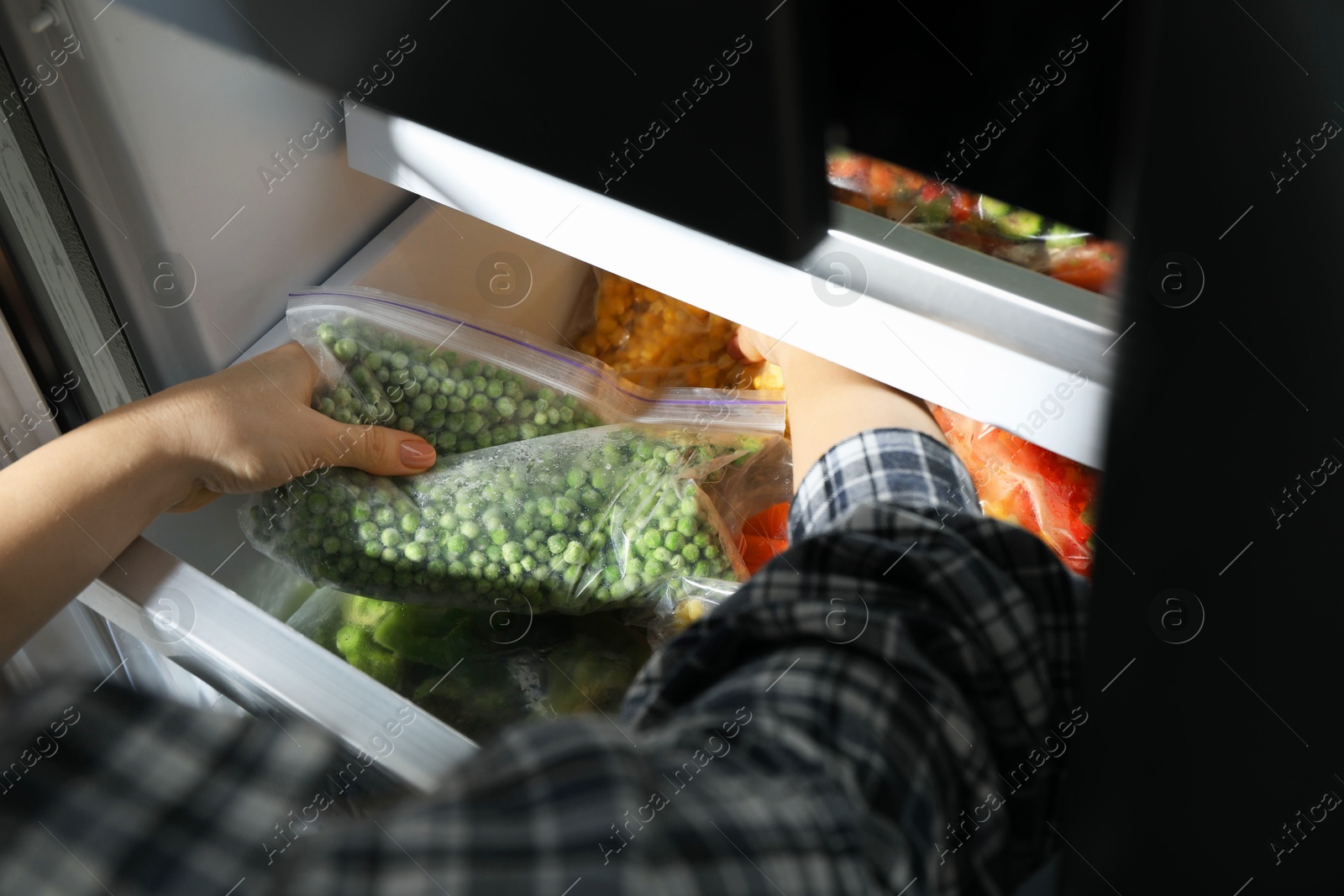 Photo of Woman taking plastic bag with frozen green peas from refrigerator, closeup