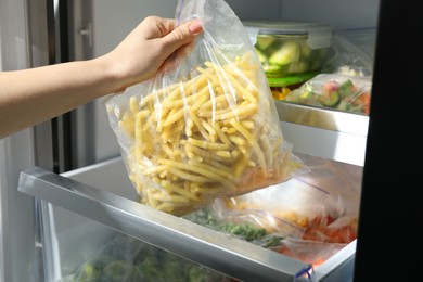 Photo of Woman taking plastic bag with frozen yellow beans from refrigerator, closeup