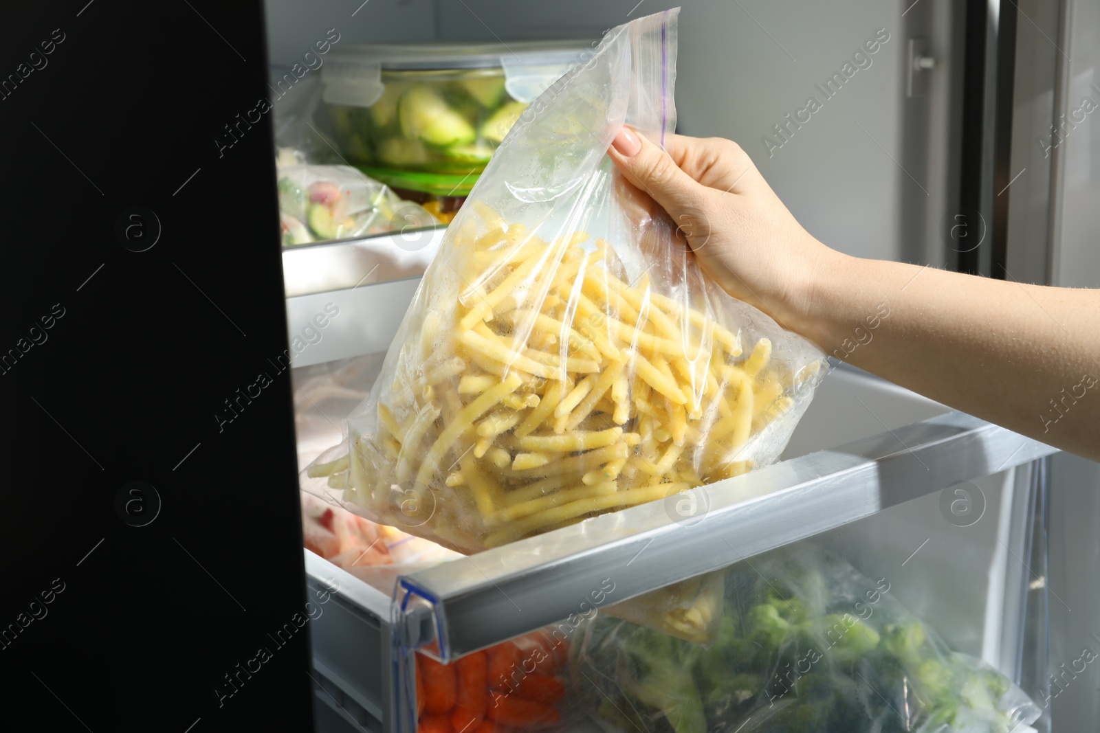 Photo of Woman taking plastic bag with frozen yellow beans from refrigerator, closeup