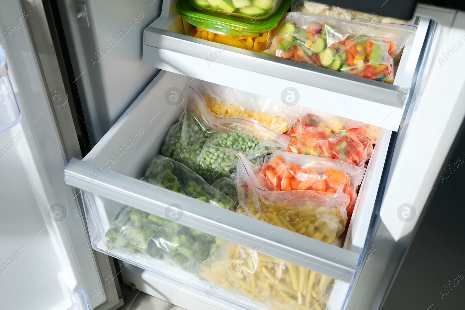 Photo of Plastic bags and glass containers with different frozen vegetables in refrigerator