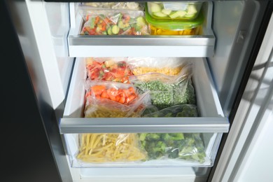 Photo of Plastic bags and glass containers with different frozen vegetables in refrigerator