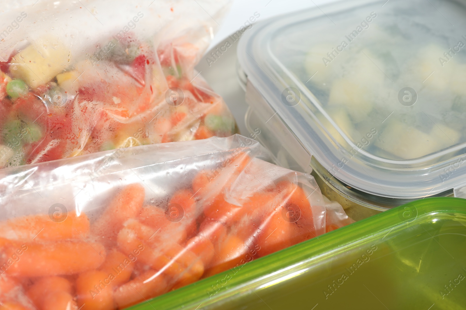 Photo of Plastic bags and glass container with different frozen vegetables in refrigerator, closeup