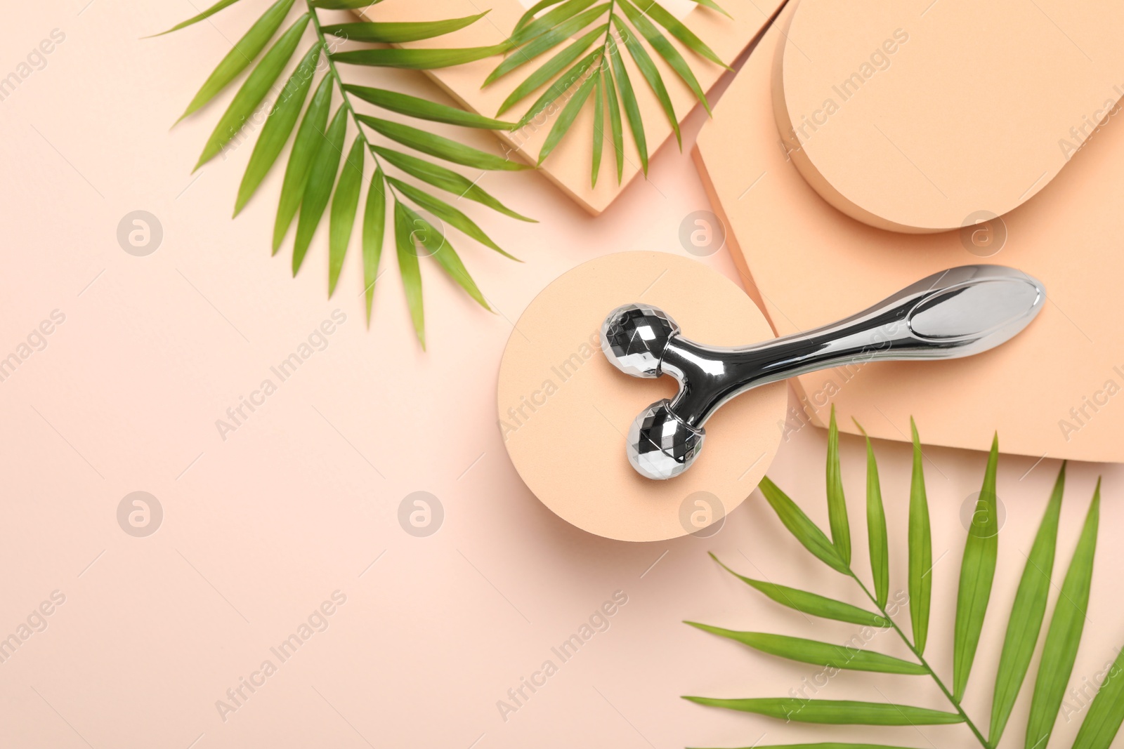 Photo of Metal face roller and palm leaves on beige background, flat lay. Space for text