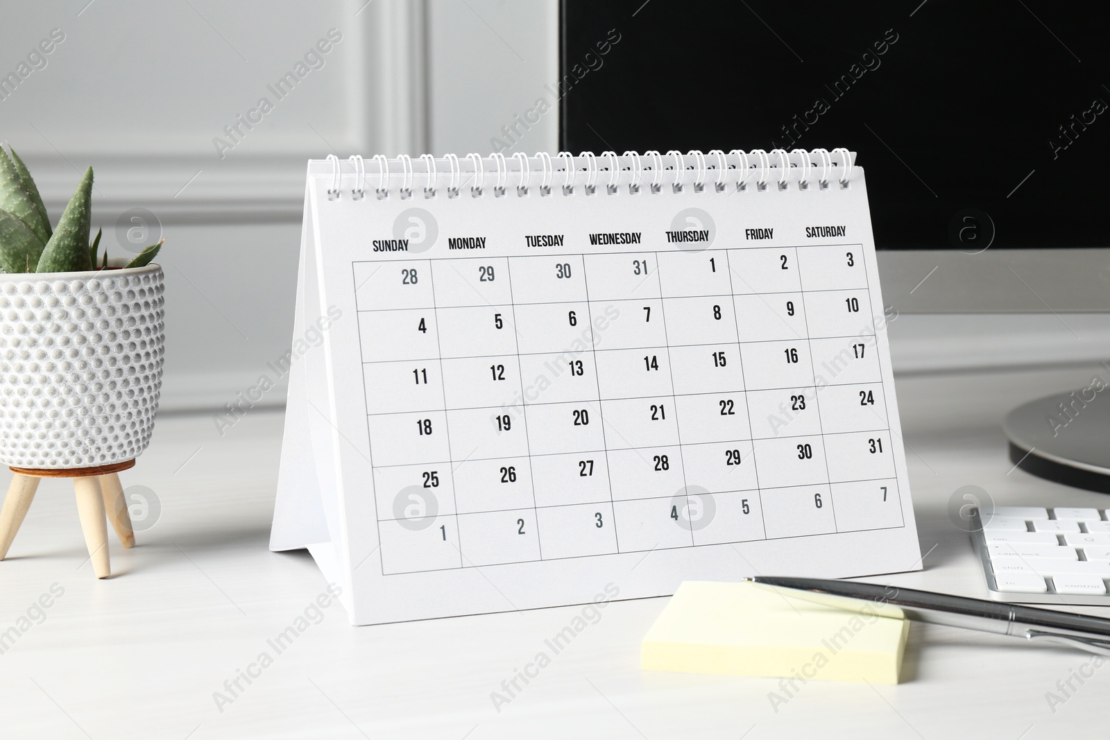 Photo of Timetable. Monthly planner, floral decor, stationery and computer on white table