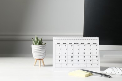 Photo of Timetable. Monthly planner, floral decor, stationery and computer on white table