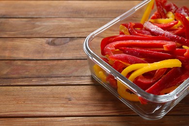 Photo of Slices of frozen bell peppers in glass container on wooden table, closeup. Space for text