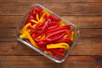 Photo of Slices of frozen bell peppers in glass container on wooden table, top view